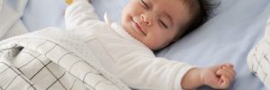 Smiling baby girl lying on a bed sleeping on blue sheets
